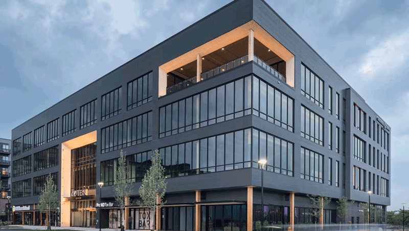 Dark five-story office building at dusk with a rooftop terrace and ground-floor storefronts